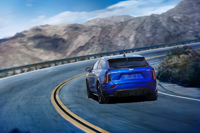 Rear View of a Blue 2026 OPTIQ-V Driving on a Curve of a Mountain Row | Dutton Cadillac in RIVERSIDE CA