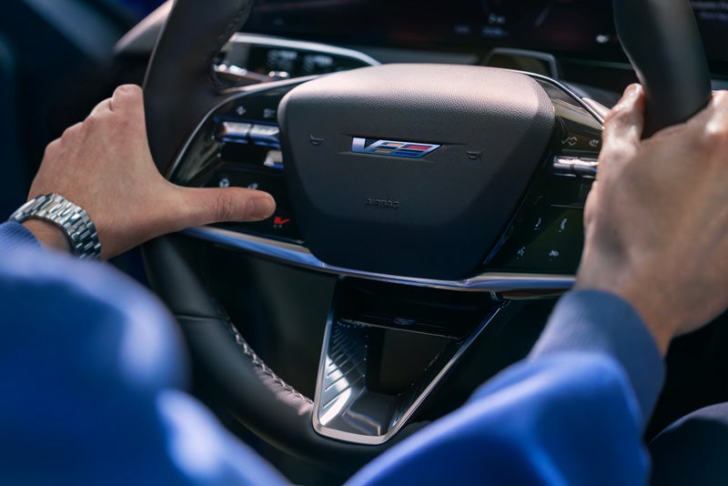 Close-up of a Man About to Press the V-Button on the 2026 OPTIQ-V Steering Wheel | Dutton Cadillac in RIVERSIDE CA