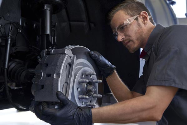 Mechanic in safety glasses and gloves installing a new brake rotor and caliper on a car.